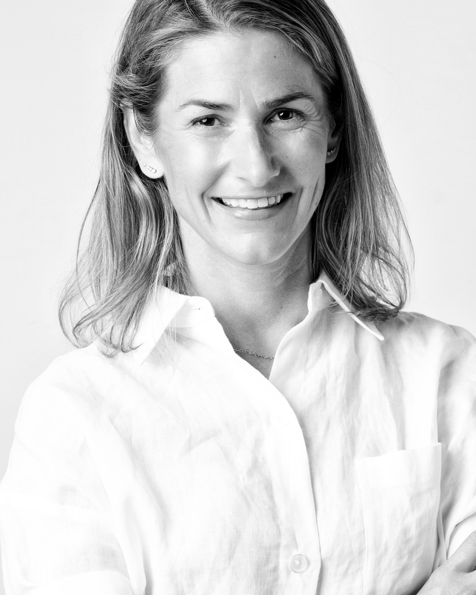 Black-and-white headshot of a smiling person with shoulder-length hair in a white linen shirt, corporate photography by Winky Lewis